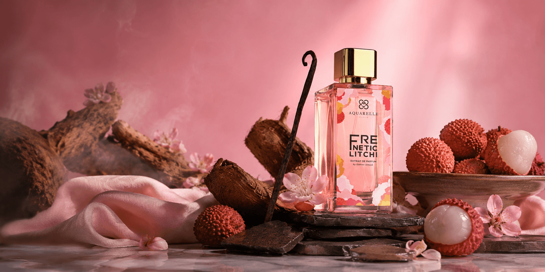Flacon de Frenetic Litchi mis en scène avec du bois flotté, des litchis, des fleurs de cerisier et un tissu rose, sur fond rose profond